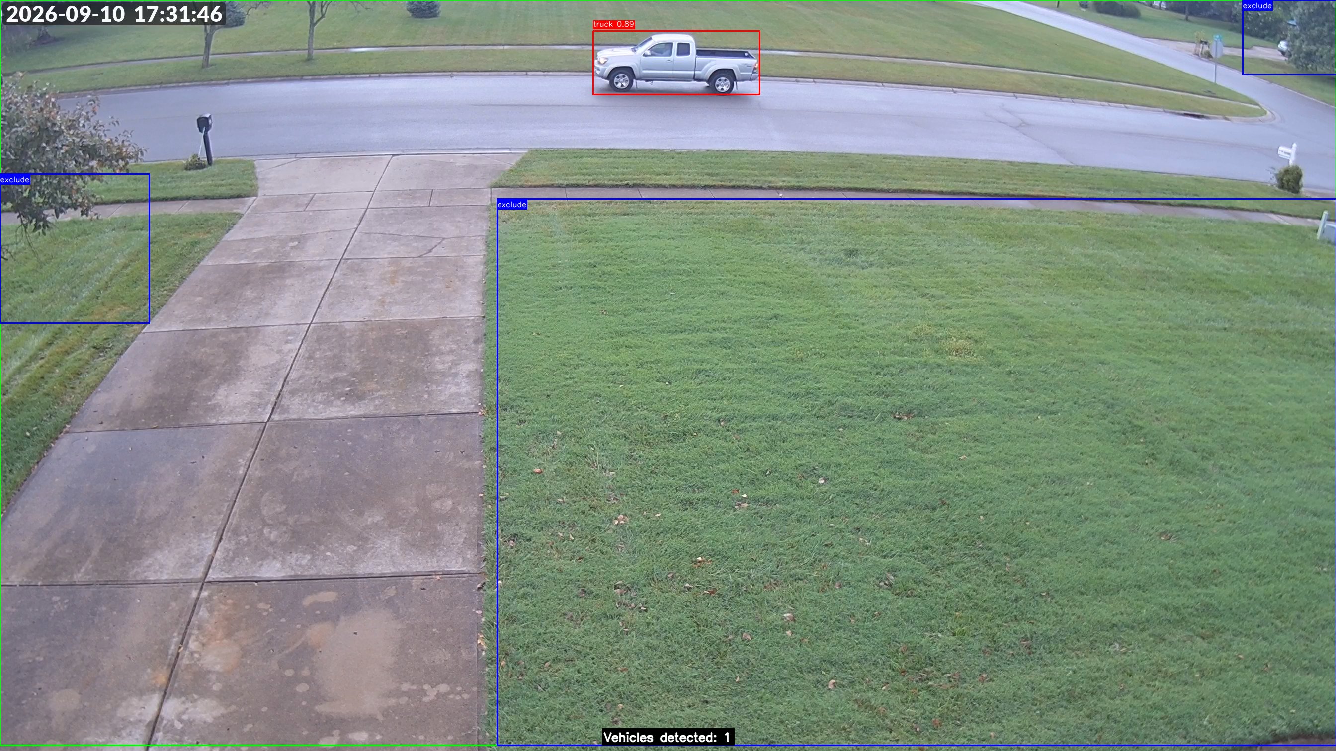 Camera view of the street in front of the house with a parked pickup truck outlined in a red detection box and lawn areas outlined in blue exclude boxes